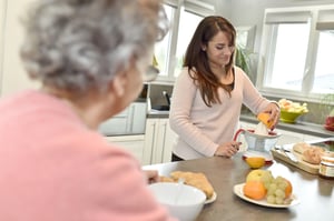 Home helper serving breakfast to elderly woman