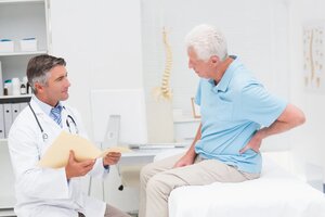 Male doctor discussing reports with senior patient suffering from back pain in clinic