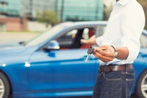 Male hand holding car keys offering new blue car on background 