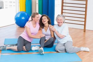 Playful female friends sitting together on exercise mat in gym