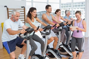 Trainer walking along people working out at elypticalclass in gym