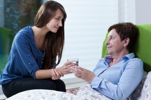 young caregiver handing water to older woman in bed