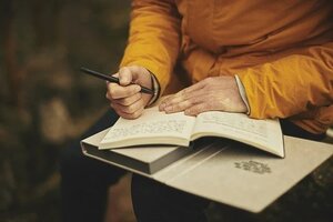 older woman writing in gratitude journal outside