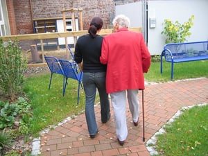 caretaker helping older woman walk through park