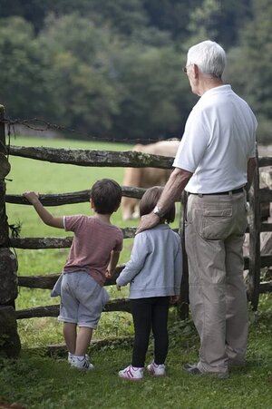 grandfather-with-grandchildren-outdoors looking at livestock on a farm