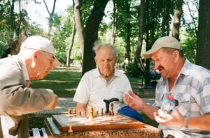 Three older men playing chess together outside in a park 