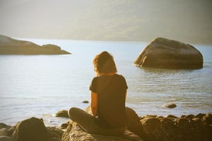 woman sitting by sea meditating