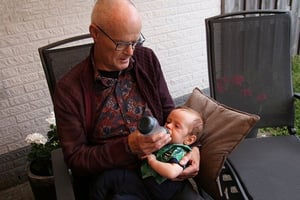 Older gentleman babysitting for young child, feeding while sitting in a chair