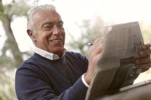 older gentleman reading a newspaper in a park 
