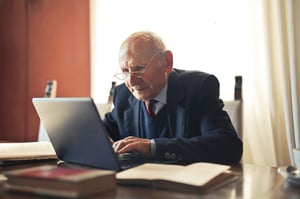 older man leaning over to see computer at desk
