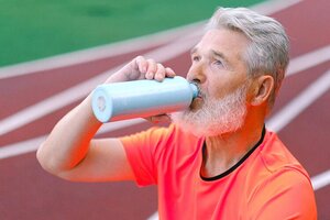 older man drinking water after workout on track