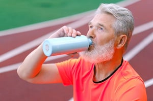 older man on running track drinking from reusable metal water bottle