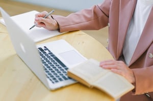 older woman reading and writing with book and laptop