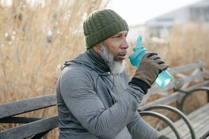 older gentleman drinking water outside on a bench