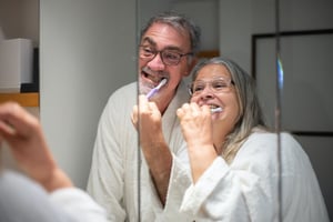 older couple brushing teeth together in the mirror 