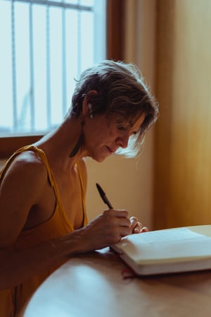 older woman writing in notebook at kitchen table