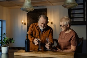 older couple in empty house pouring glass of wine