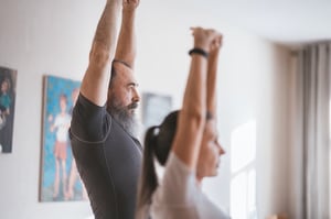 Older man and woman stretching in living room together