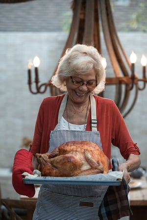 grandmother bringing cooked turkey to table for Thanksgiving dinner