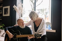 older man playing guitar with his wife