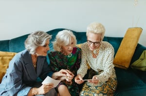 three older women friends sharing a couch looking at photo