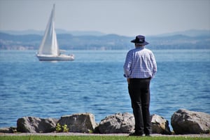 older man sttanding by see watching sailboat