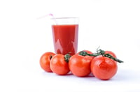 four tomatoes in front of glass of fresh tomato juice